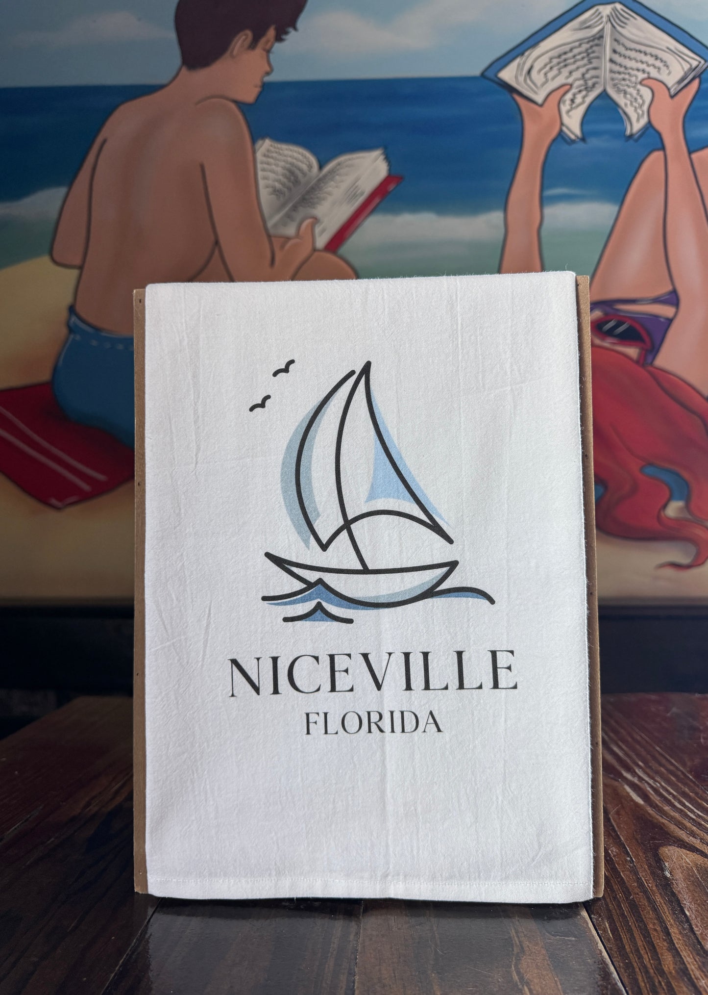 White towel with sailboat design and 'Niceville Florida' text on a table with a beach scene in the background.