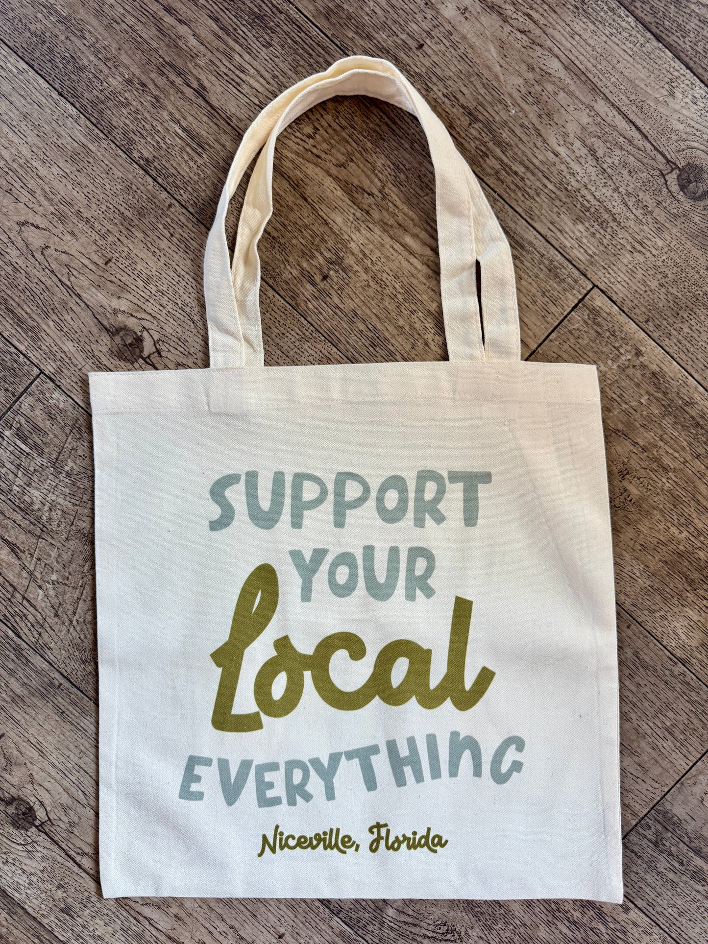 Tote bag with 'Support Your Local Everything' text on a wooden surface