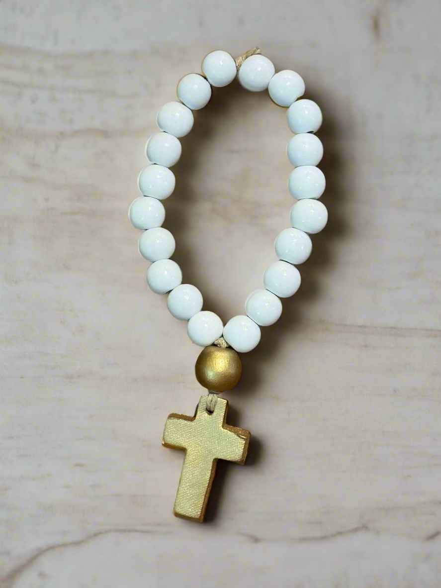 White beaded bracelet with a gold cross pendant on a marble background