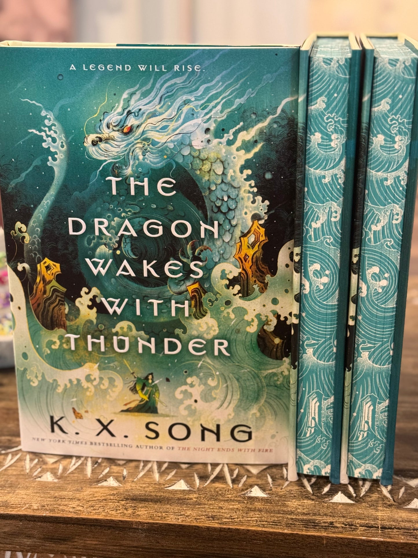 Book titled 'The Dragon Wakes with Thunder' by K.X. Song on a wooden surface.