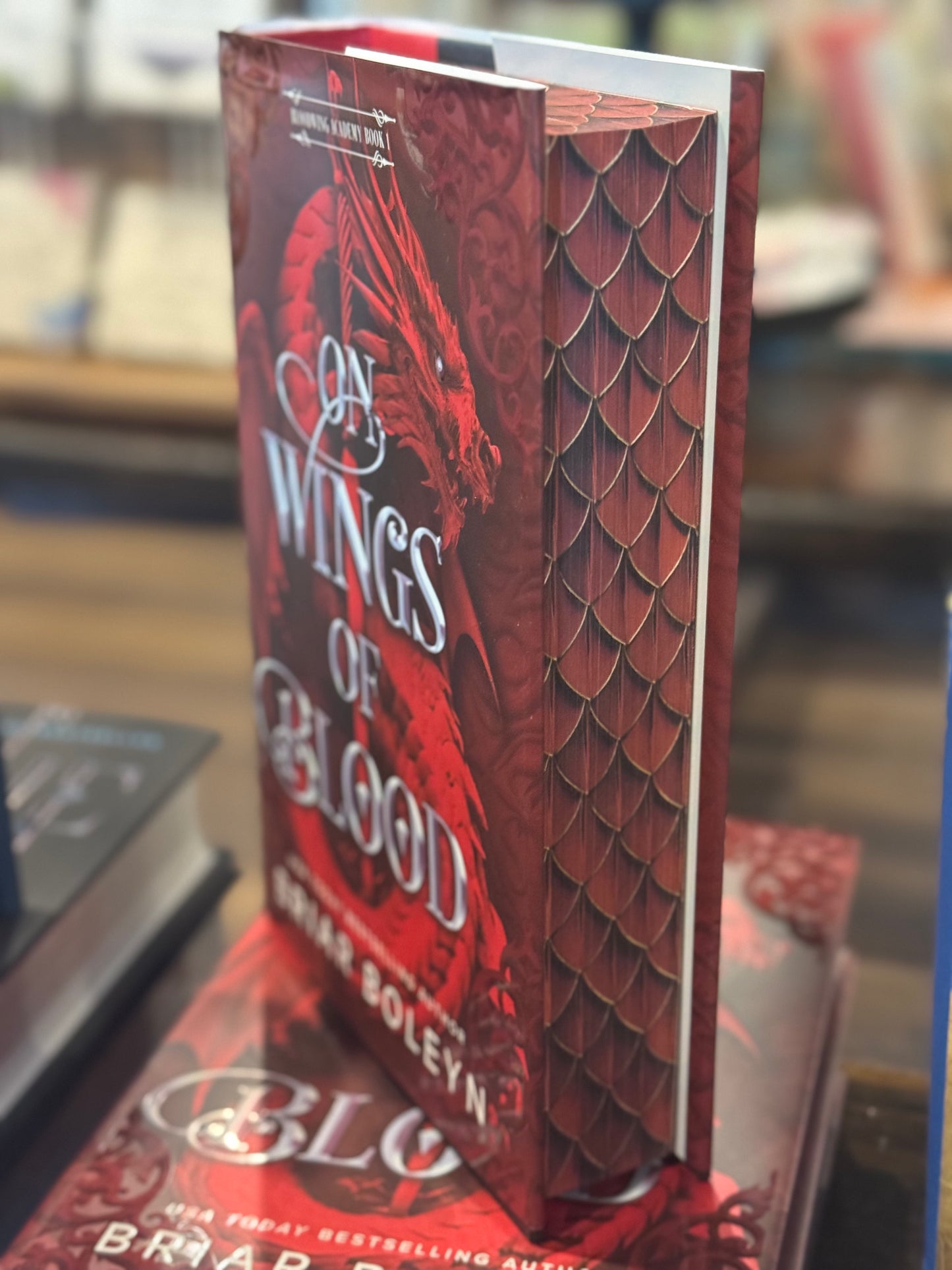 Book titled 'On Wings of Cold Blood' with a red dragon design on the cover, placed on a surface.