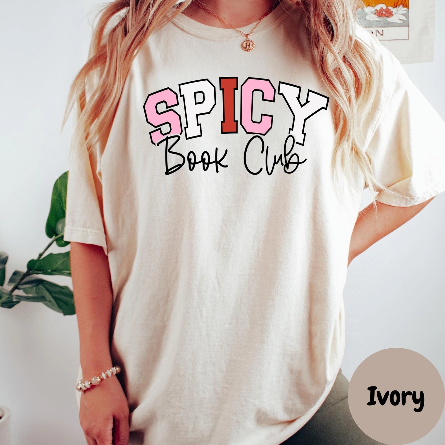 Person wearing a 'Spicy Book Club' t-shirt with a plant and white wall in the background