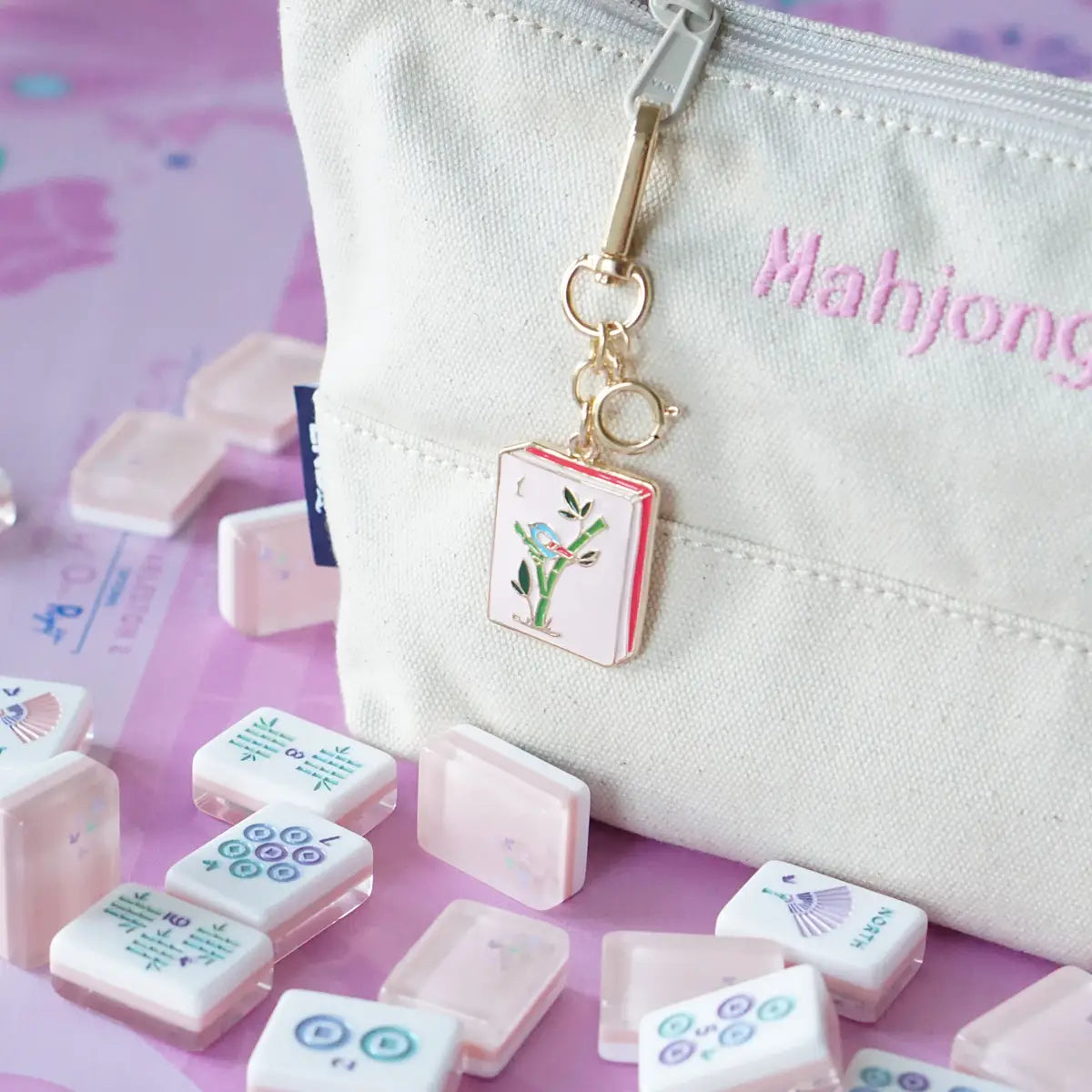 White pouch with 'Mahjong' text and keychain, surrounded by mahjong tiles on a pink background