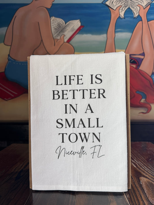 Textile with 'Life is better in a small town Niceville, FL' on a wooden surface with a mural in the background.