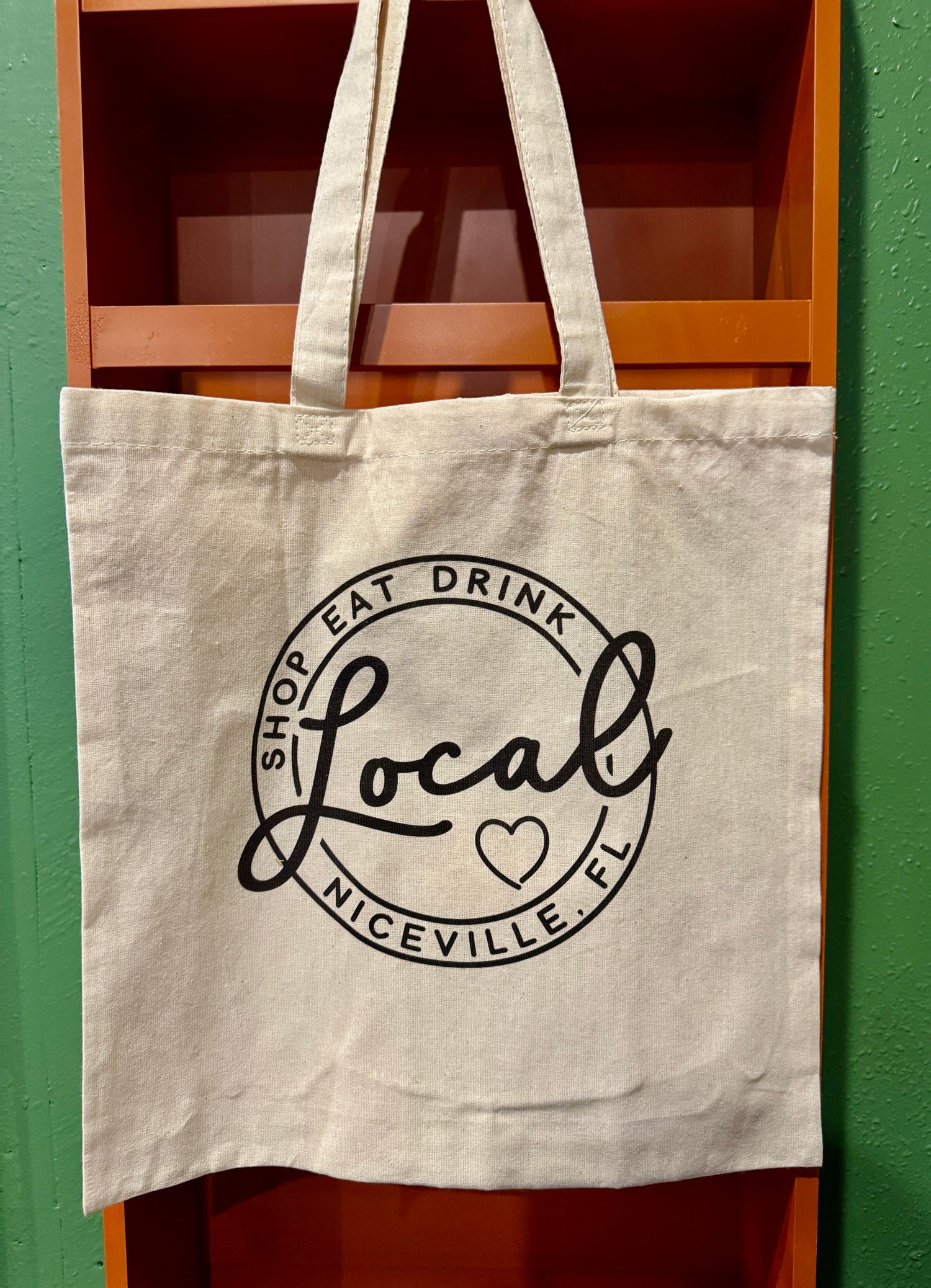 Beige tote bag with 'Shop Eat Drink Local Niceville, FL' text on a green and brown background