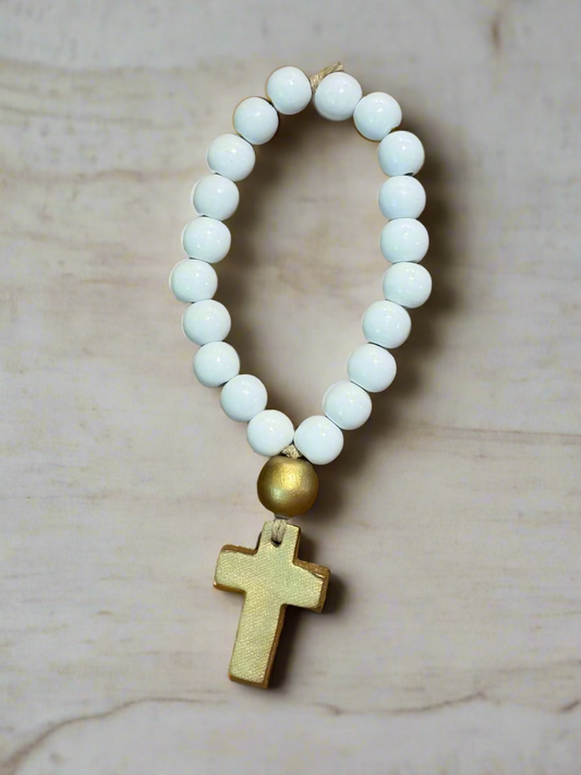 White beaded bracelet with a gold cross pendant on a marble background