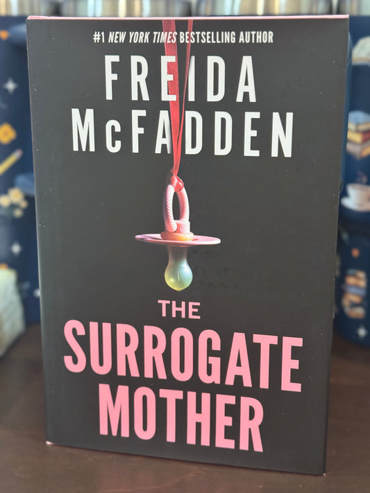 Book cover of 'The Surrogate Mother' by Freida McFadden with a pacifier graphic on a dark background.