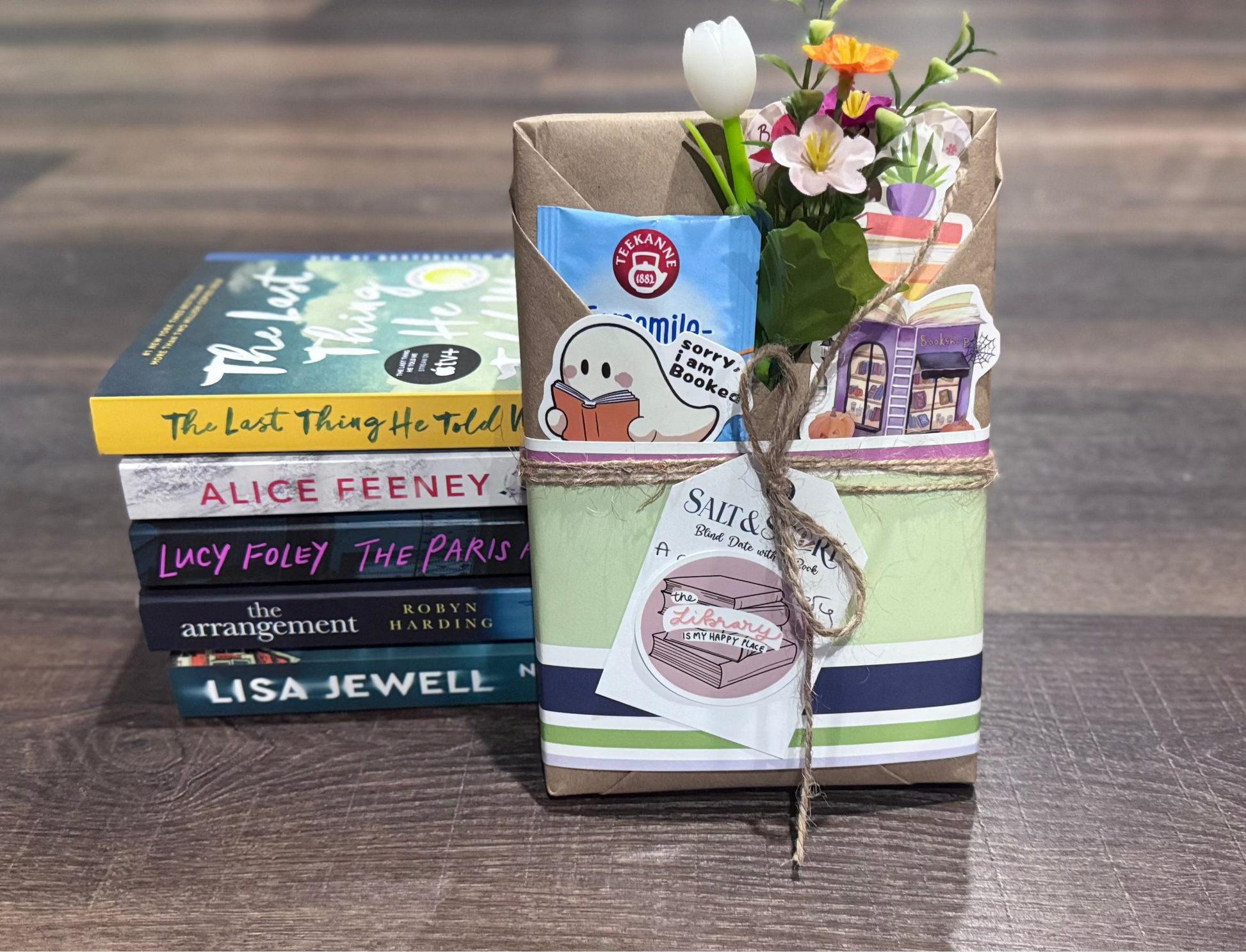 Stack of books and a gift bag with flowers on a wooden surface