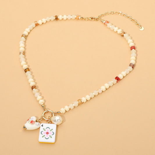 Necklace with beaded chain and floral charm on a beige background