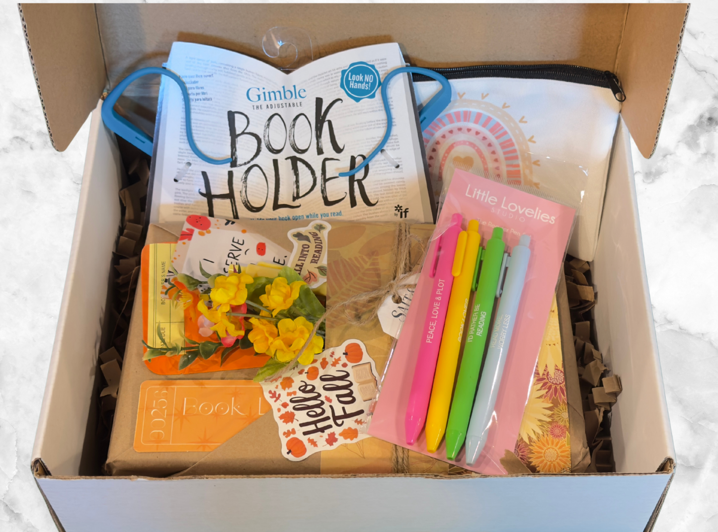 Box containing stationery items including a book holder, colorful bookmarks, and a card with 'Hello Fall' text.