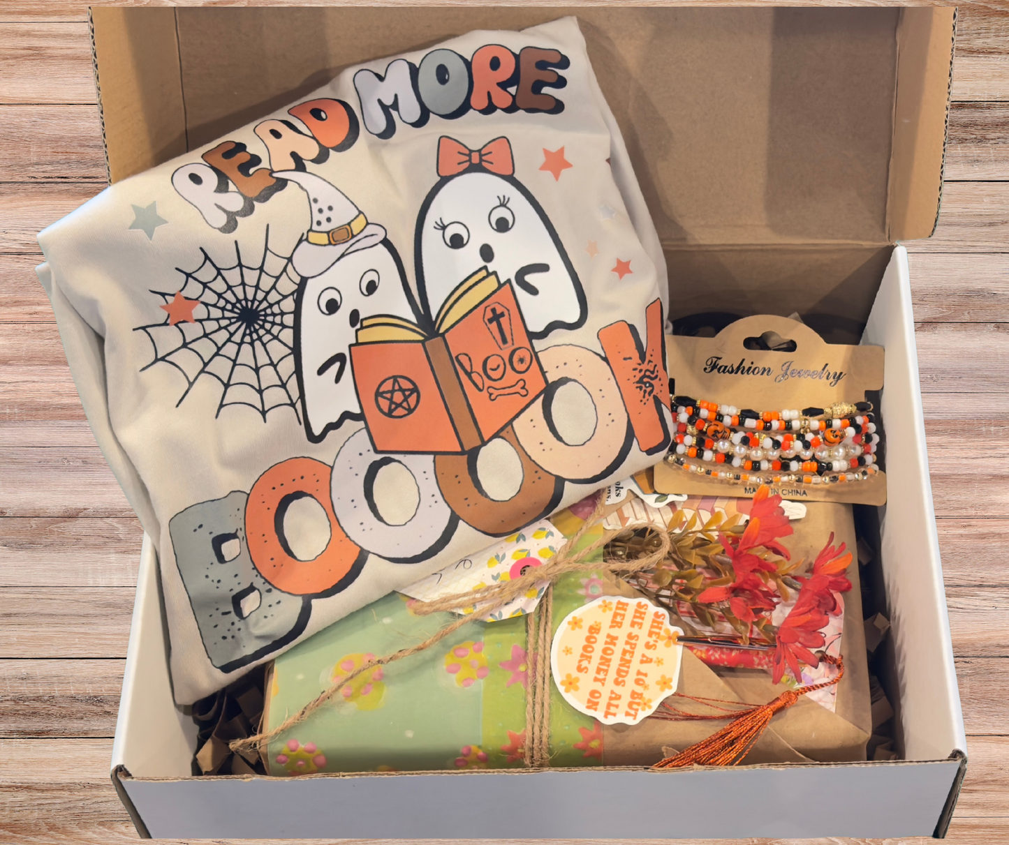 Open box containing a Halloween-themed t-shirt, decorative items, and jewelry on a wooden surface.