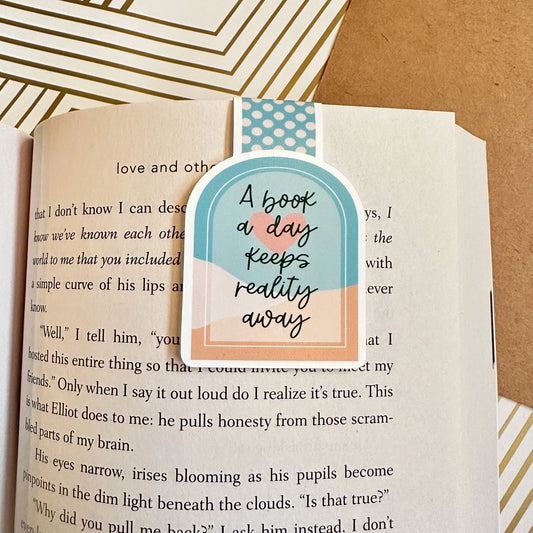 Bookmark with 'A book a day keeps reality away' text on an open book.