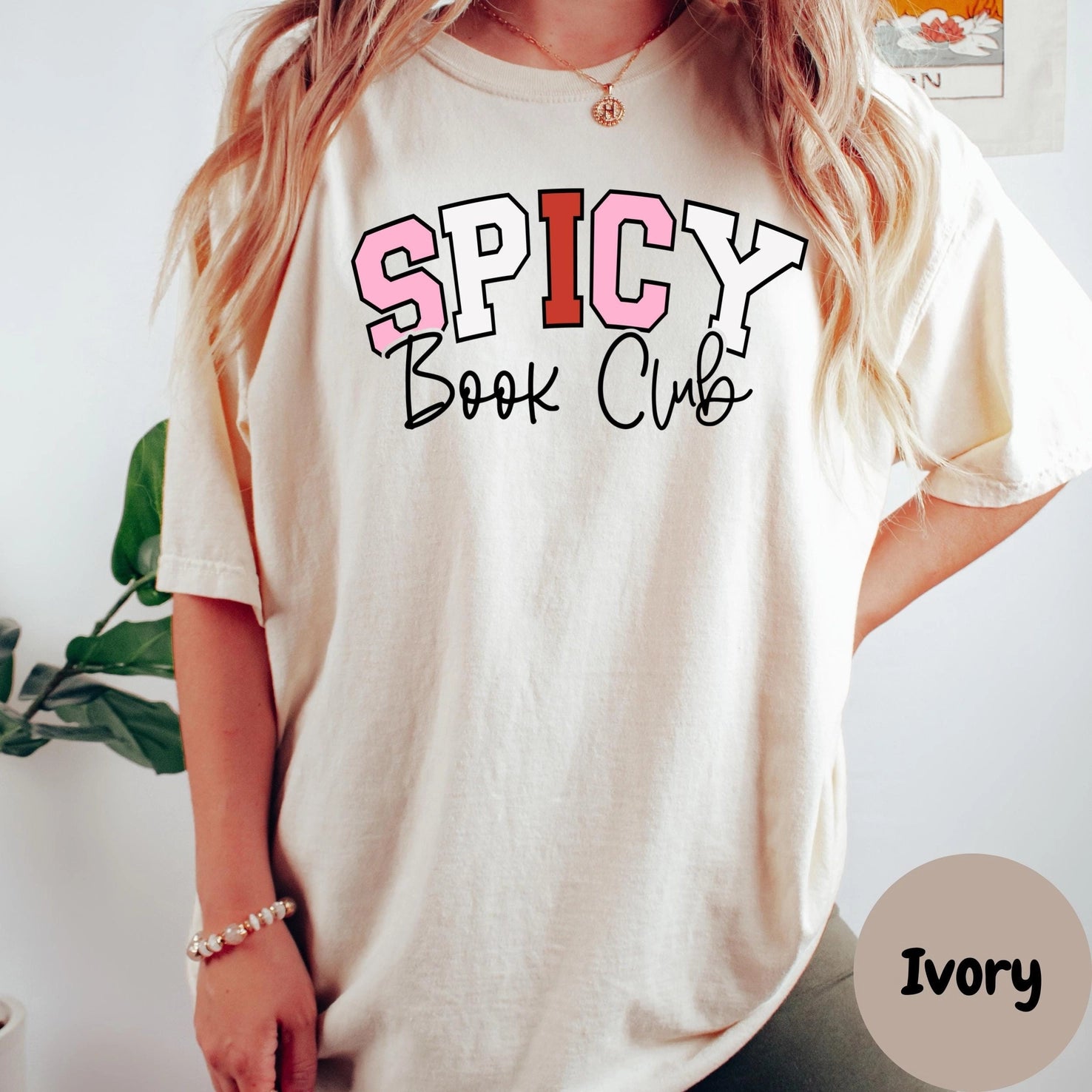 Person wearing a 'Spicy Book Club' t-shirt with a plant and white wall in the background