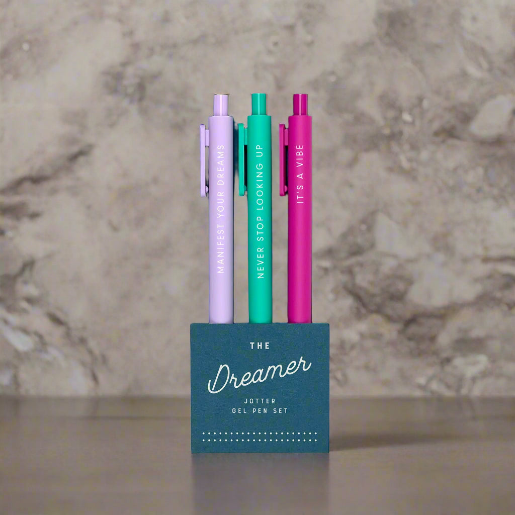 Set of three gel pens in purple, green, and pink with motivational text in a blue packaging on a white background.